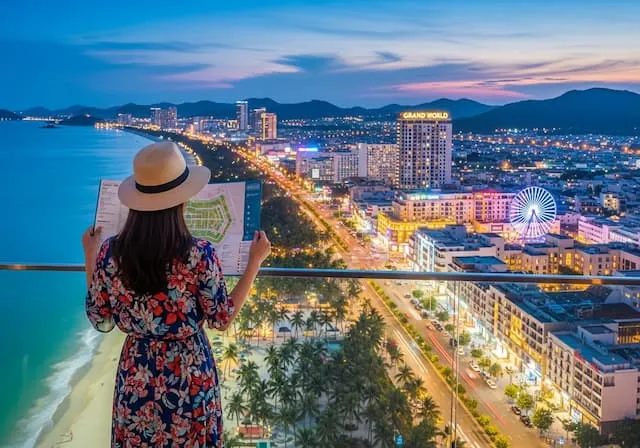 푸꾸옥 북부의 화려한 그랜드 월드 야경과 남부의 투명한 에메랄드빛 켐 비치 바다를 배경으로, 호텔 지도를 보며 고민하는 30대 한국인 여성 여행자의 뒷모습